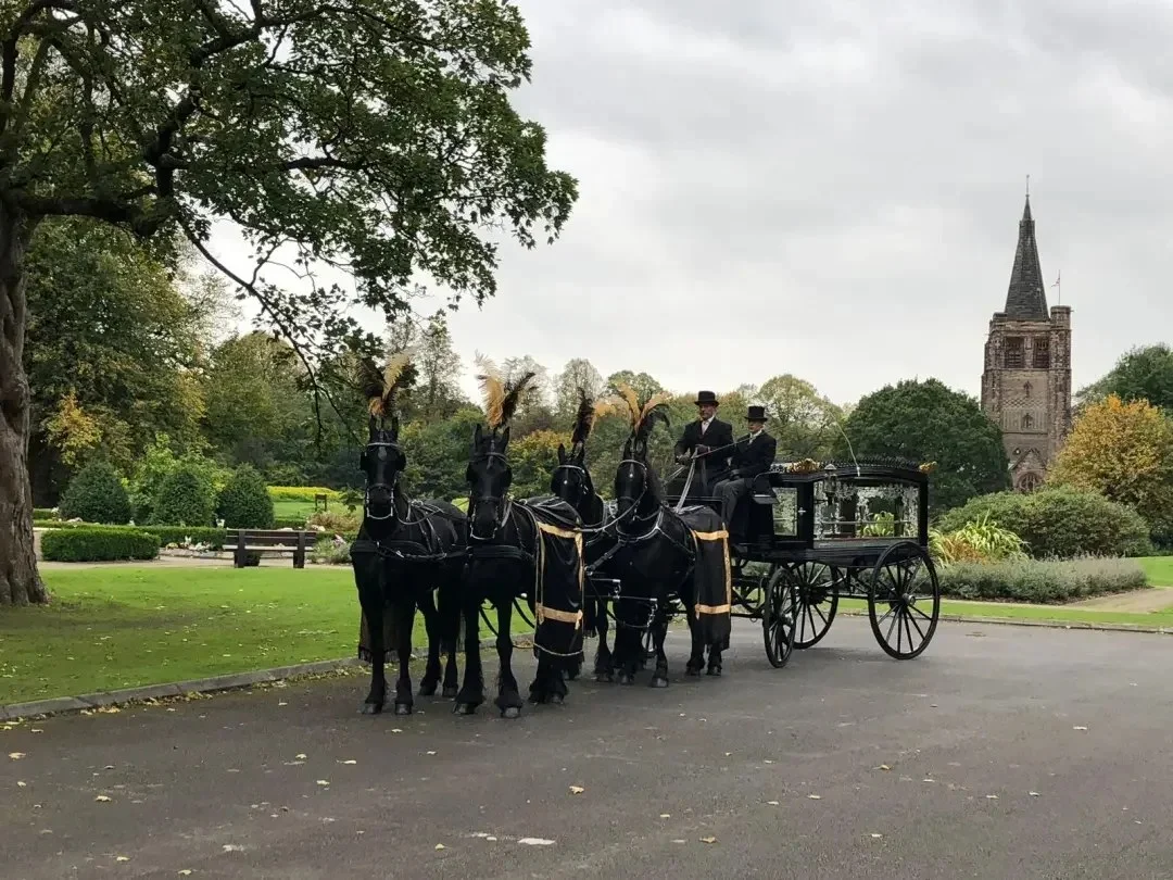 Team of black horses drawing a hearse near a church spire